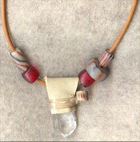 White buckskin wrap over Arkansas quartz crystal; accented wih red glass crow beads and sandcast beads on a 30